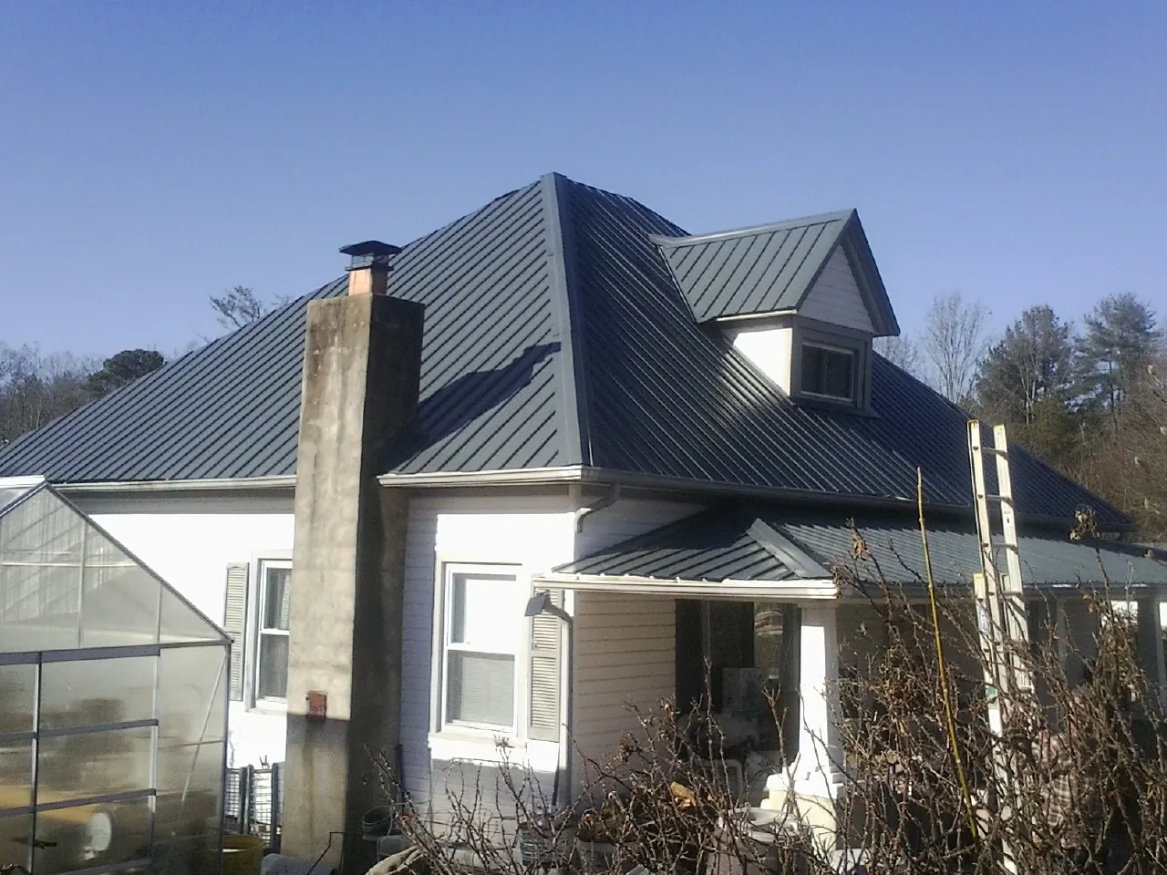Dark blue standing seam metal roof on a white farmhouse with dormer — Slate & Tile Roof Repair by Roofing Brothers in Lind