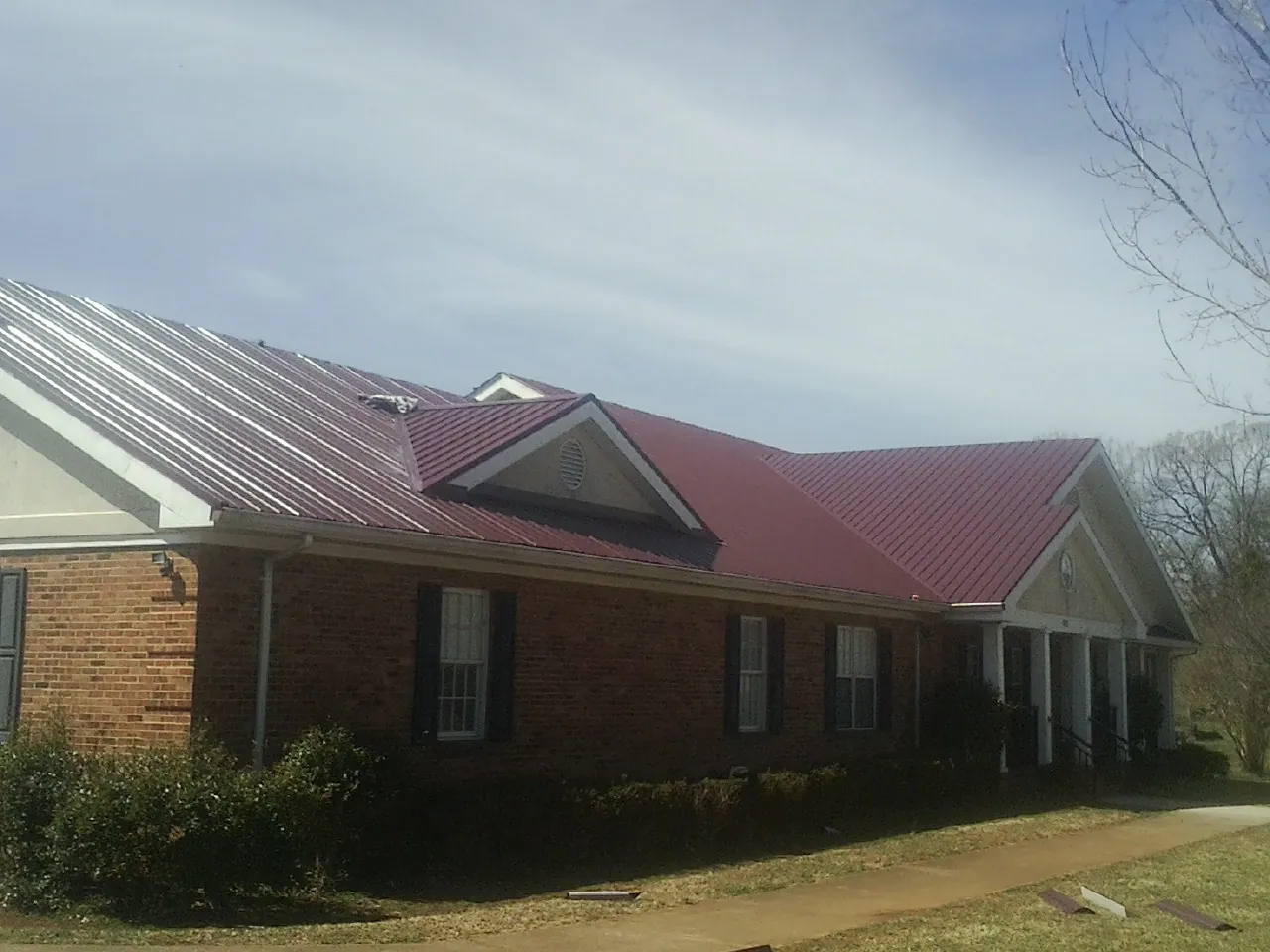 Red metal roof with gabled entries on a long brick building, from a Hail Damage Roof Repair job in Lind