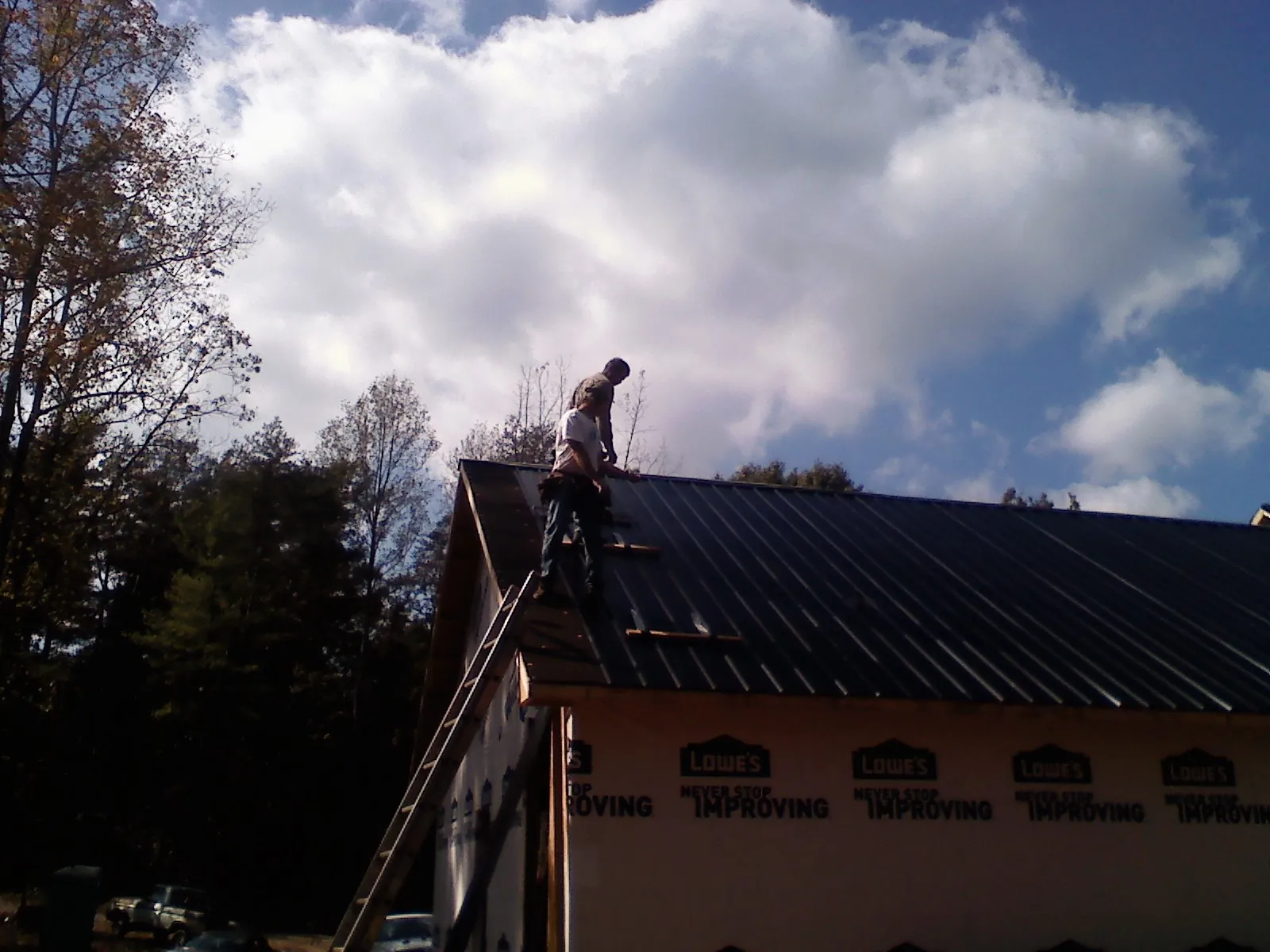 Roofer fastening dark metal panels high against a cloudy sky in Lind