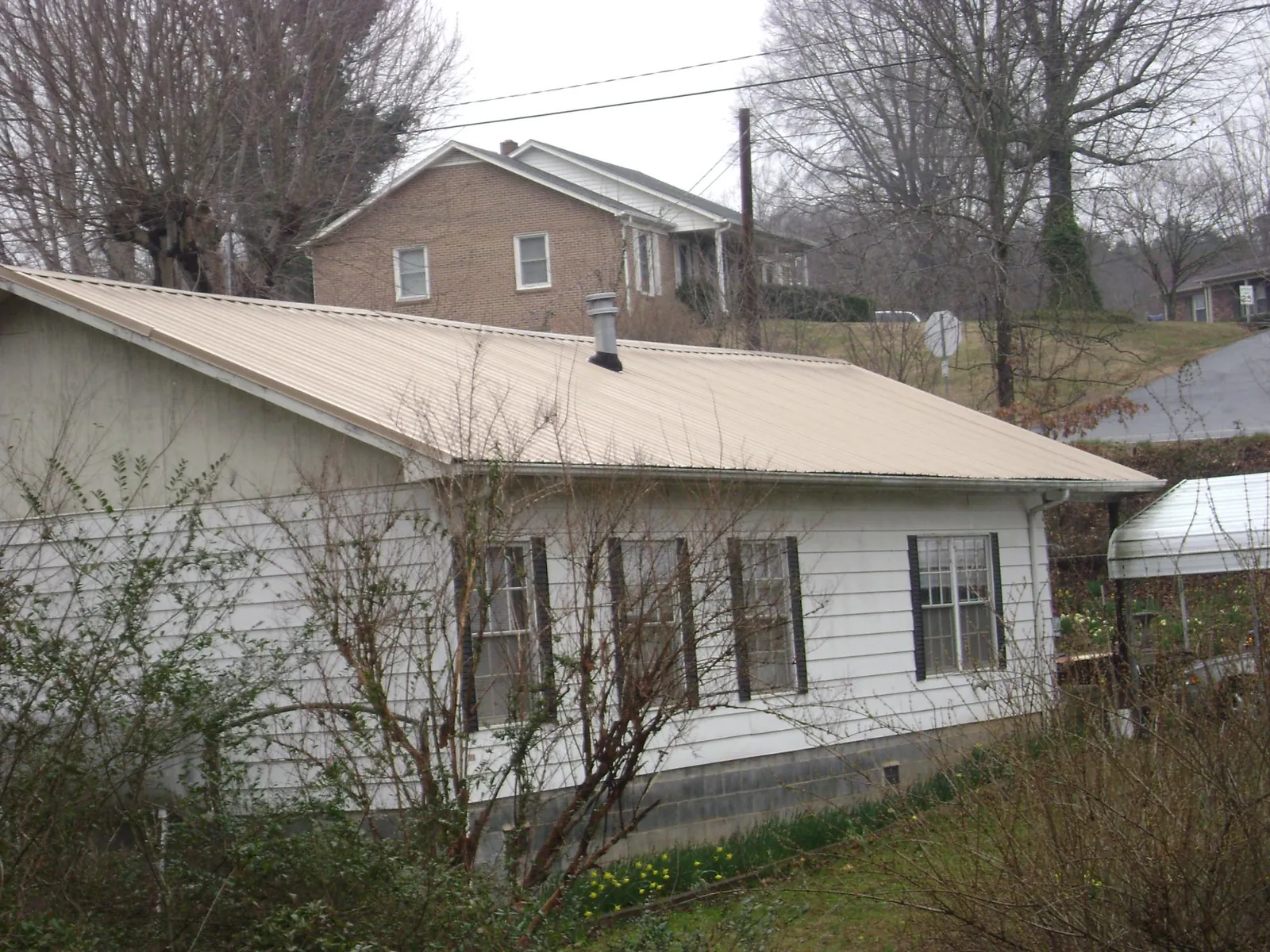 Tan metal roof on a white sided house set into a hillside — Commercial Roofing by Roofing Brothers in Lind