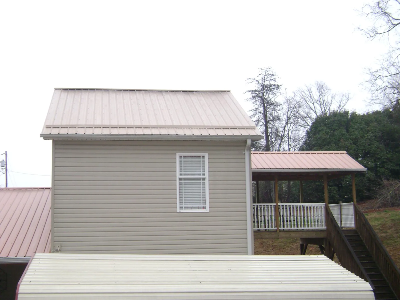 Tan metal roofs on a two story addition and attached porch, from a Roof Replacement job in Lind